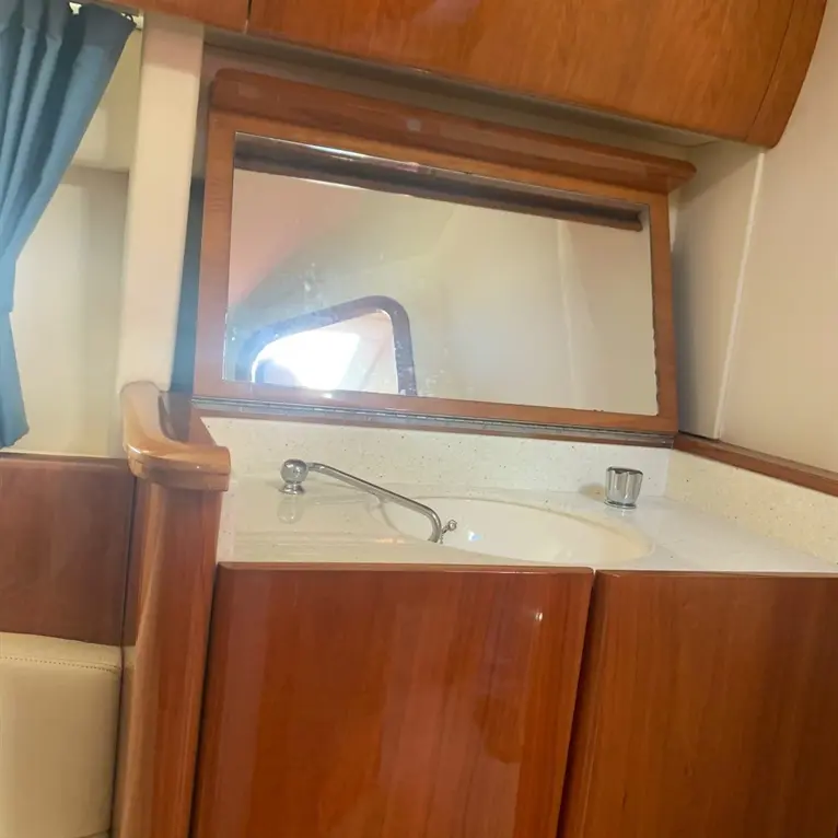 Modern boat bathroom with wooden cabinetry, sink, mirror, and blue curtains providing privacy. Bright and clean atmosphere.